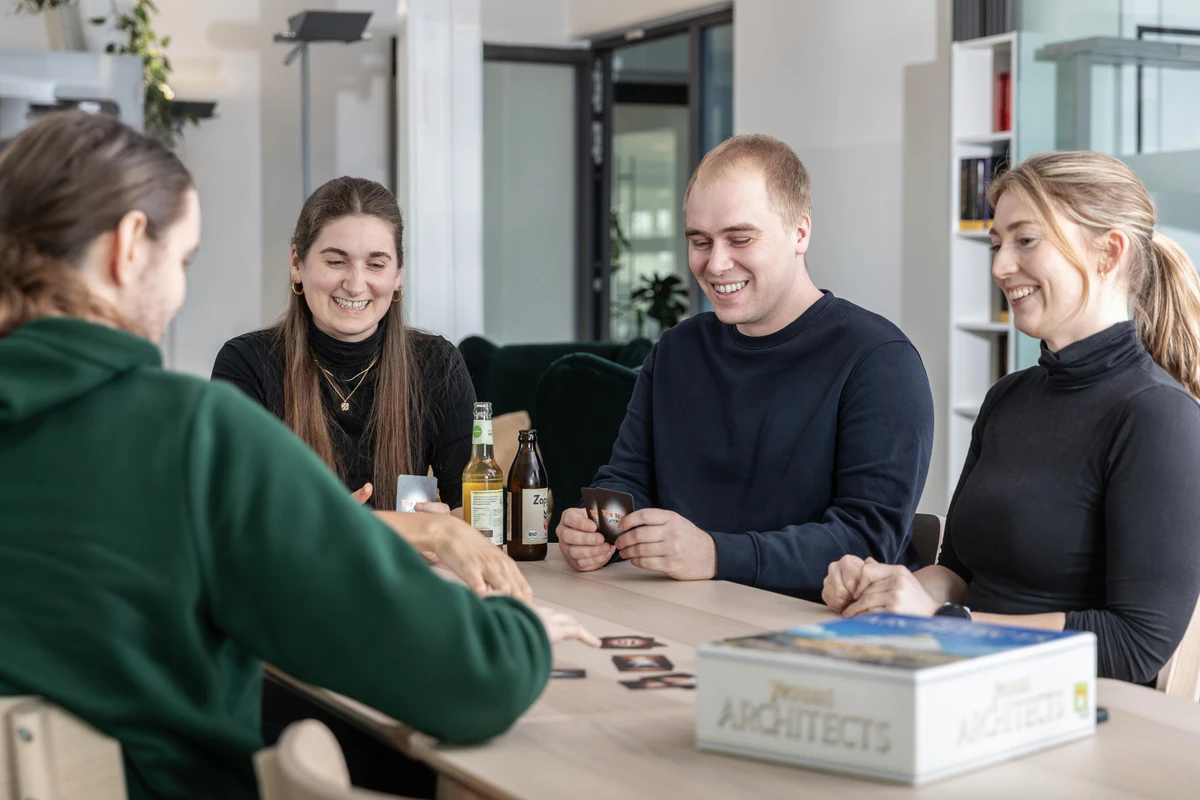 Mitarbeitende von Heringer Consulting sitzen entspannt zusammen im Büro und spielen nach Feierabend gemeinschaftlich ein Gesellschaftsspiel. Starker Teamzusammenhalt und gelebte Unternehmenskultur