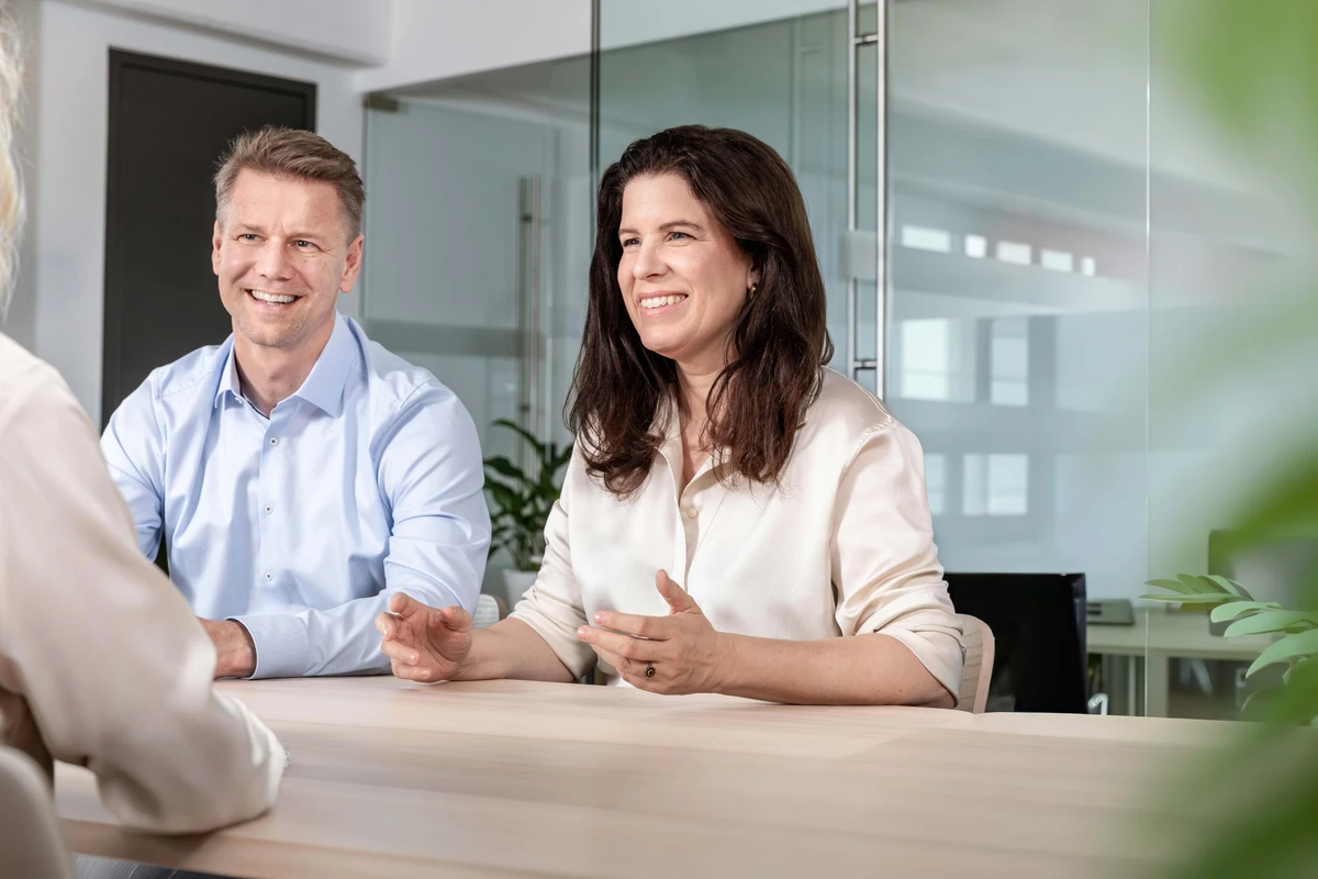 Ein Beraterteam von Heringer Consulting im sympathischen, fachlichen Gespräch mit einem Kunden an einem Besprechungstisch. Erfolgreiche Datenprojekte durch starke Partnerschaft