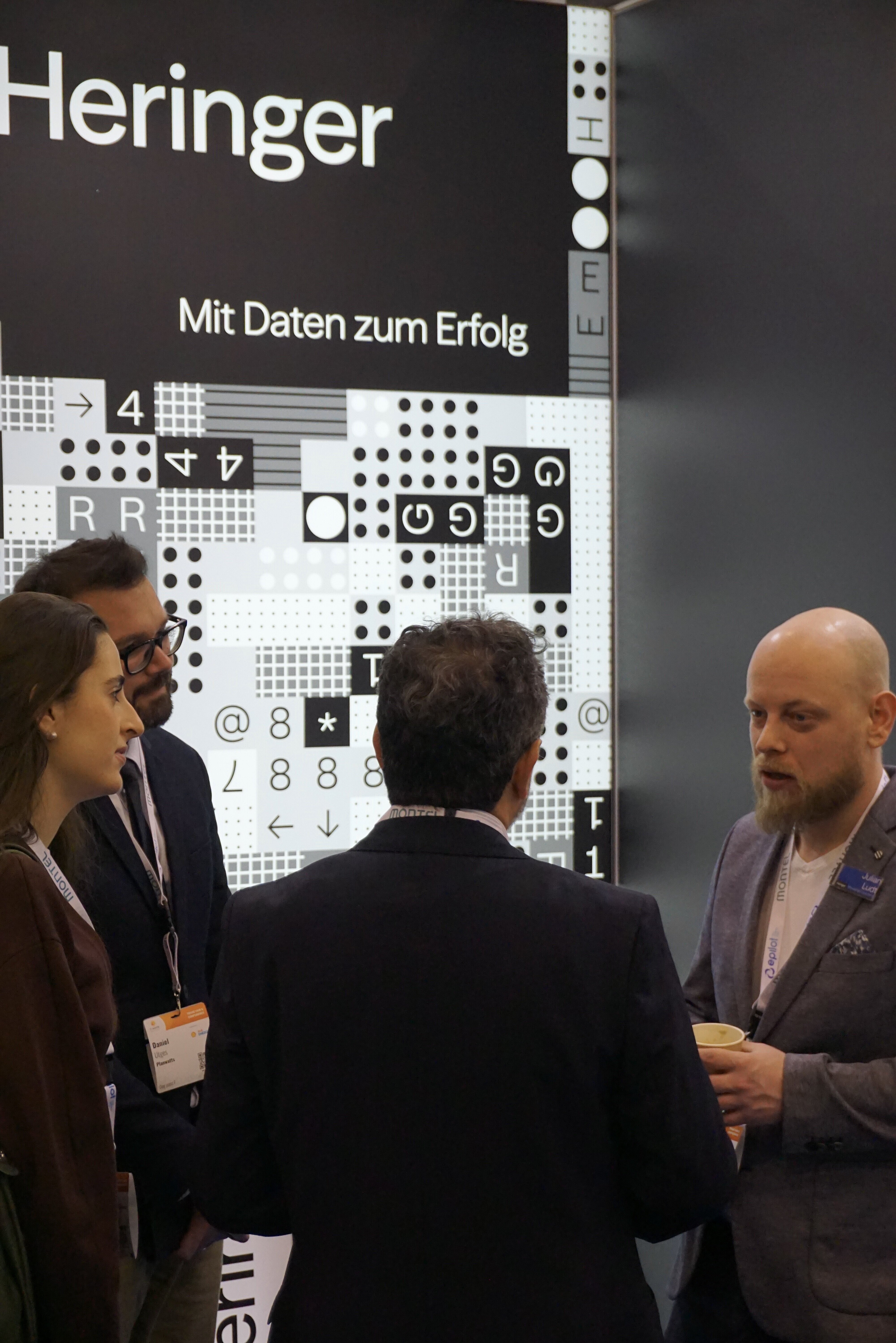 Vier Personen im Gespräch am Messestand der Heringer Consulting GmbH mit Claim „Mit Daten zum Erfolg“